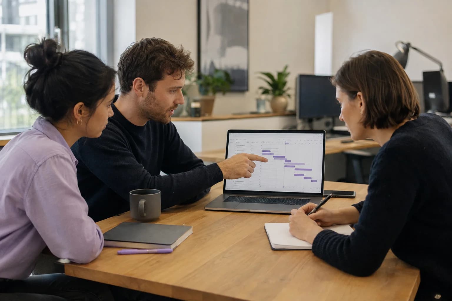 Three colleagues reviewing a project timeline together at a laptop.